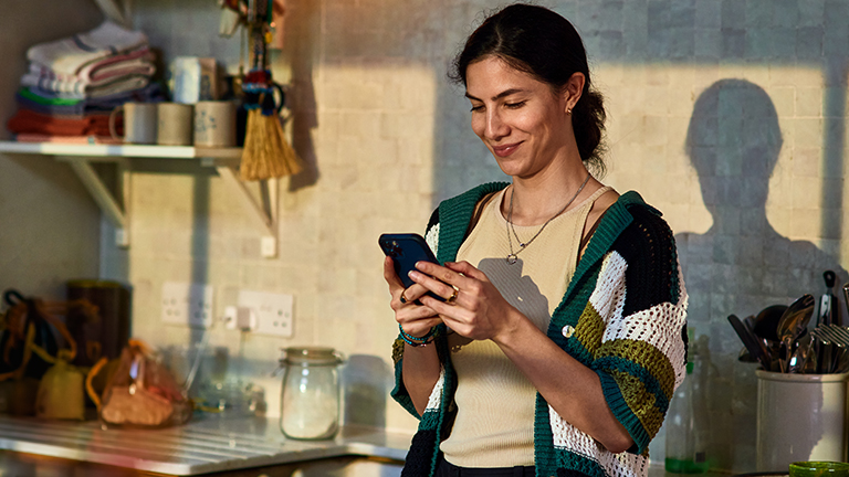 Vrouw leunt tegen aanrecht met mobiel in de hand