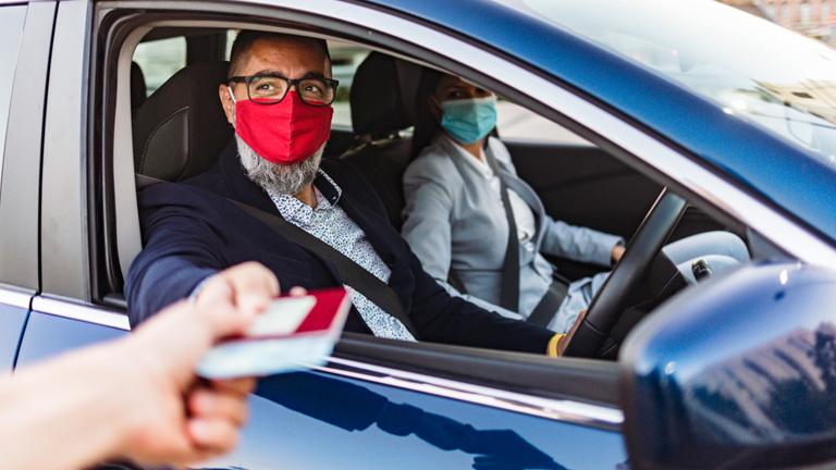 Man en vrouw in de auto met mondkapje bij grens oversteekpunt